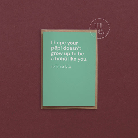 Greeting card with text 'I hope your pēpi doesn’t grow up to be a hōhā like you. congrats btw' on a mint green background, placed on a contrasting surface