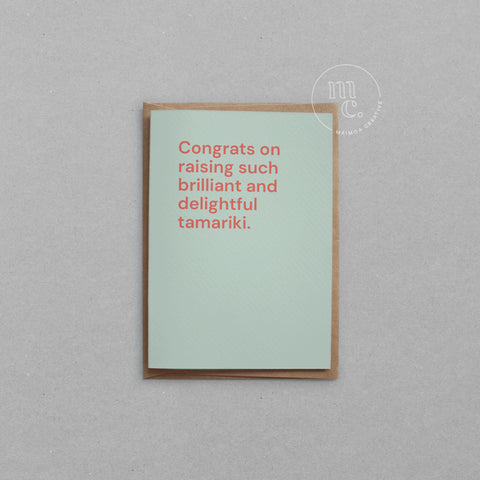 Greeting card with text 'Congrats on raising such brilliant and delightful tamariki' on a light mint background, placed on a light surface