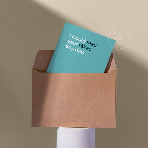 Cheeky card peeping from a kraft envelope on a plinth with the text 'I would mau your rākau any day.' against a beige background.