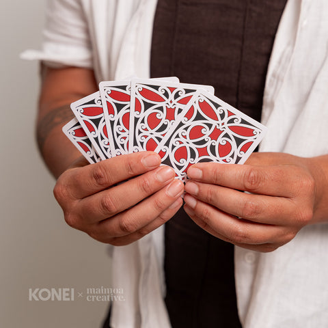 Close-up of hands holding intricately designed playing cards featuring black, red and white Māori designs, emphasising their cultural uniqueness and authenticity.