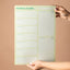 Person holding a green magnetic weekly planner with 'Mahere ā-wiki' text on a brown background