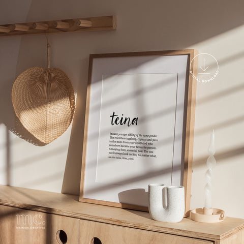 Framed teina definition print on a wooden sideboard in warm natural light, styled with minimalist decor. Reo Māori family term wall art.