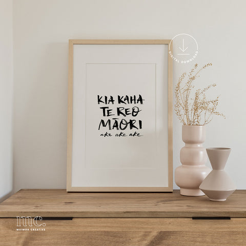 Framed print with hand-lettered text "Kia kaha te reo Māori ake ake ake" on a wooden shelf with decorative vases.