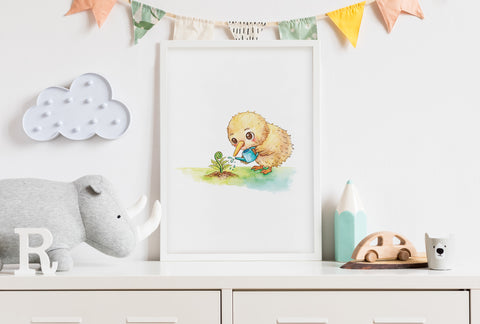 A framed print of a cute watercolour illustration of a fluffy kiwi chick gently watering a young fern frond in a nursery room on a dresser