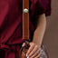 Person holding a brown leather bag with a 'Tangata Tiriti' gold pin wearing a dark plum outfit