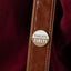Brown leather strap with a gold and white 'Tangata Tiriti' badge pin on a plum background