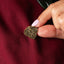 Hand holding a gold decorative tiki pin against a maroon fabric background