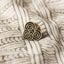 Decorative tiki gold pin with on a textured Māori design fabric background