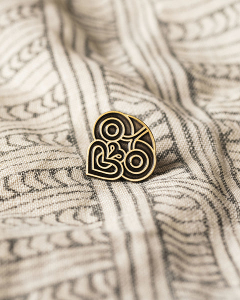 Decorative tiki gold pin with on a textured Māori design fabric background