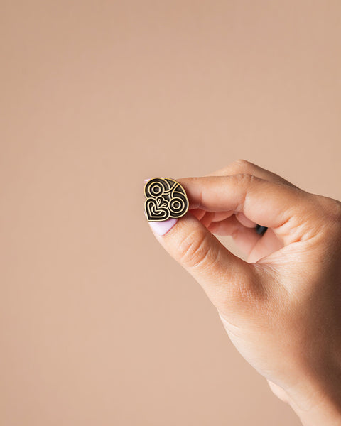 Hand holding a small decorative tiki pin on a beige background