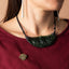 Close-up of a person wearing a pounamu and decorative tiki gold pin and a maroon top.