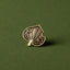 Antique gold kawakawa leaf brooch pin on a green background