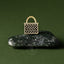 Gold woven kete basket pin on a dark greenstone pounamu surface with a green background