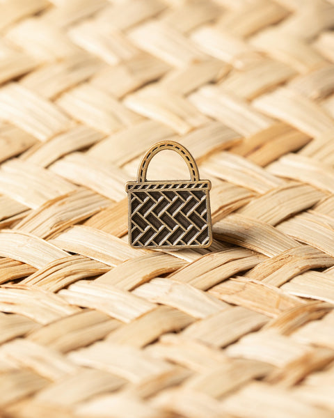 Bronze kete basket pin on a woven harakeke background