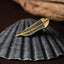 Gold huia feather brooch on a dark textured shell with a brown and wooden background