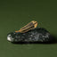 Gold huia feather brooch on a dark green stone pounamu against a green background