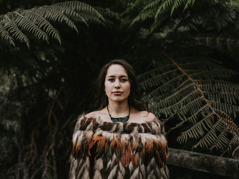 Māori woman wearing korowai and taonga with ferns in background