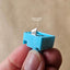 Blue blade holder for circle cutter, held between fingers against a beige background.