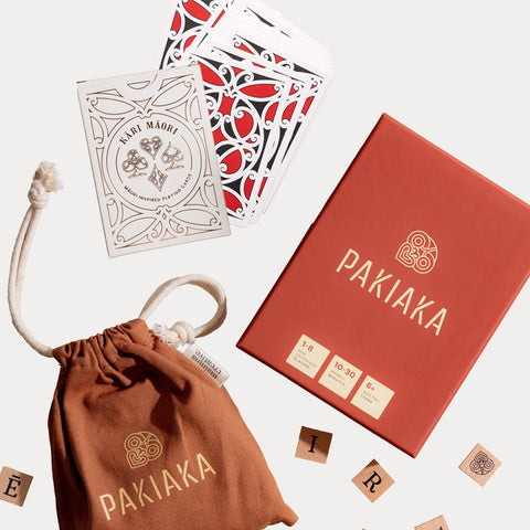 Pakiaka word game and Kāri Māori playing cards bundle displayed with game boxes, a cotton drawstring bag, and wooden letter tiles on a white background