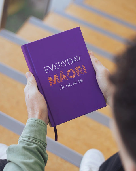 Purple notebook journal titled 'Everyday Maori ia rā ia rā' held by a person with a blurred background