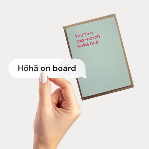 Hand holding a vinyl decal with "Hōhā on board" in a speech bubble design, over a greeting card with "You're a top-notch hōhā-hoa" message.