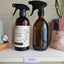 Two amber glass spray bottles on a white shelf, with the label 'kū horoi - cleaning products' in te reo māori stuck to the shelf