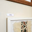 A framed Māori art piece with a white frame and a small label reading 'tāpare' in te reo Māori mounted on a wall