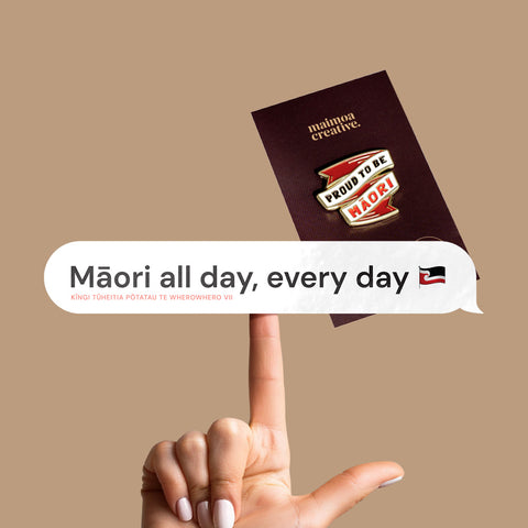 Hand holding a vinyl decal with "Māori all day every day" in a speech bubble design, with a bold 'Proud to be Māori' enamel pin in the background