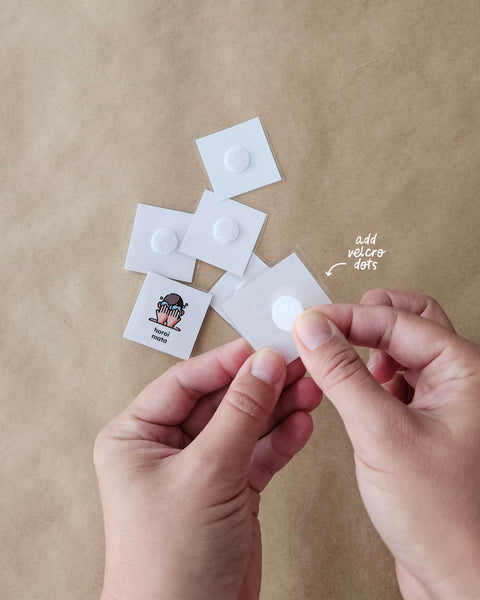 Hands holding a small white routine card adding a velcro dot to it