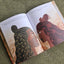 Open book with illustrations of Tāne Mahuta and Hineahuone on a textured green surface, illustrated by Isobel Joy Te Aho-White