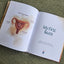 Open book showing a diagram of a female reproductive system and text 'My First Ikura' on a textured green background, illustrated by Isobel Joy Te Aho-White