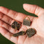 Hand holding four gold pins with different designs against a green background
