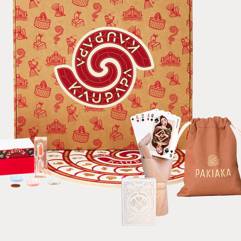 Kaupapa Game, Pakiaka word game and Kāri Māori playing cards bundle displayed with game boxes, game board pieces, timer, a cotton drawstring bag, playing cards in mannequin hand, on a white background