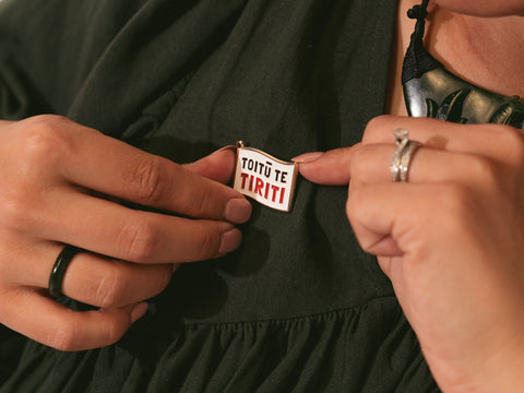 Person attaches a "Toitū te Tiriti" enamel pin to their dark green dress